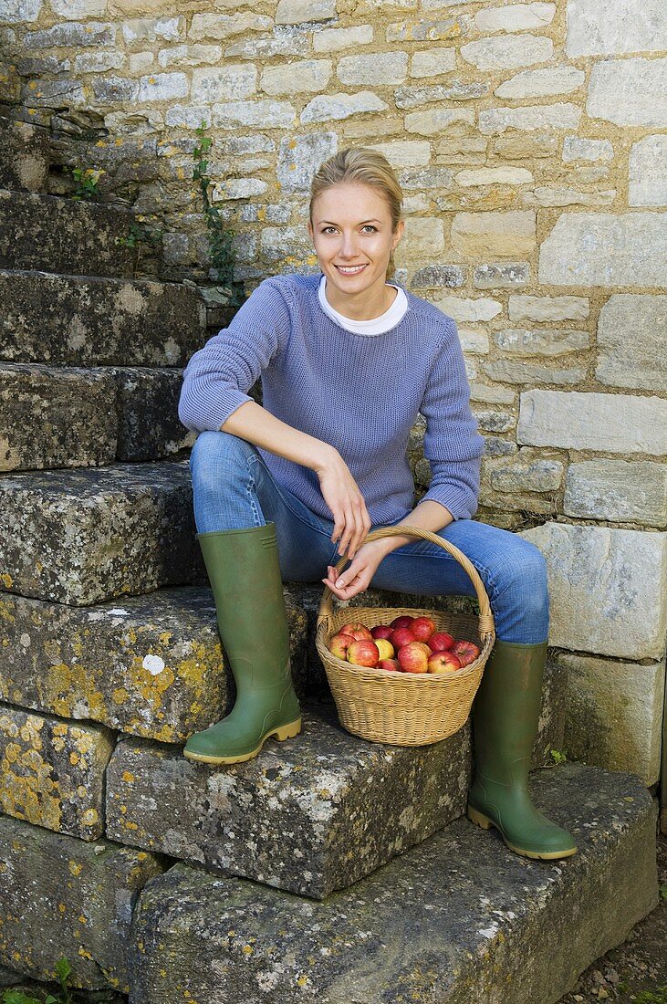 A woman sitting on a flight of stairs with a basket of apples