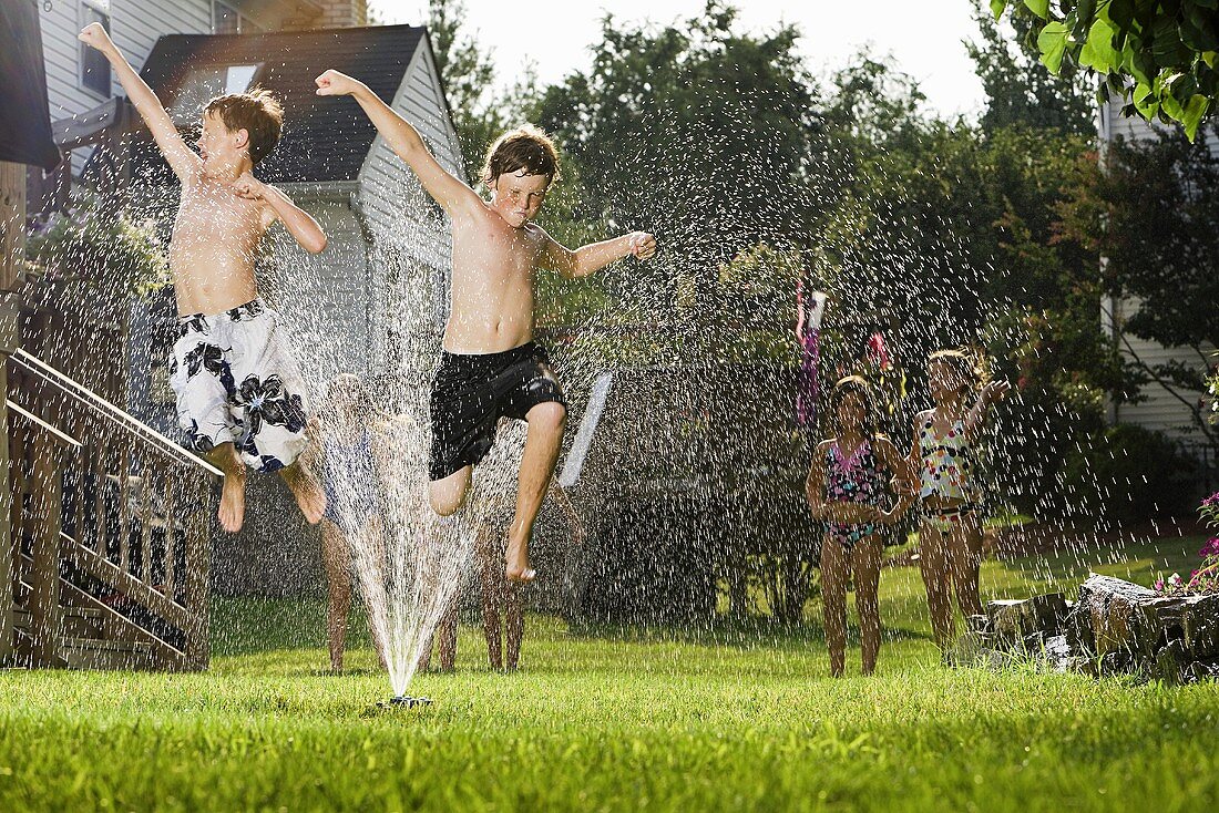 Children jumping through a sprinkler
