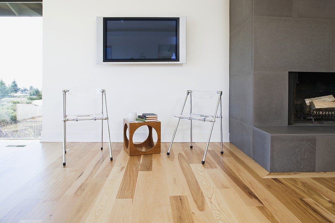 Wohnzimmer mit Kamin, Parkettboden & Plexiglas-Stühlen mit Beistelltischchen unter aufgehängtem Flachbildschirm