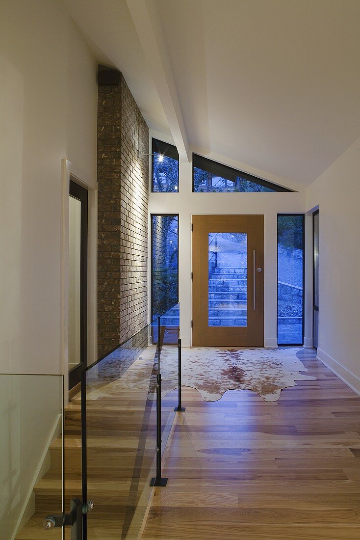 Flurbereich eines Hauses mit Parkett, Tierfellvorleger & Treppenabgang mit Glasgeländer