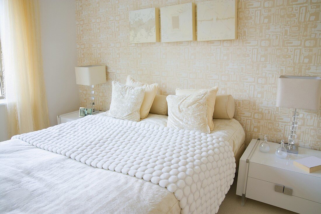 Schlafzimmer in Weiß mit Doppelbett, Nachttischchen, Tischleuchten & weiss gemusterter Wandtapete