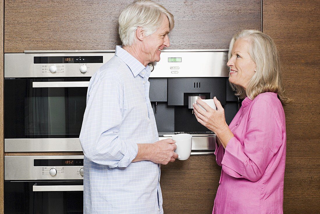 Ehepaar mittleren Alters steht in der Küche mit Kaffeetassen