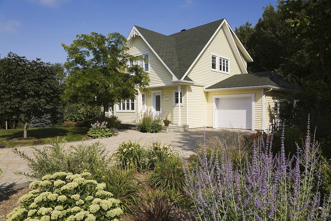 Cremefarbenes Einfamilienhaus mit blühendem Sommergarten und einer breiten, gepflasterten Garagenauffahrt