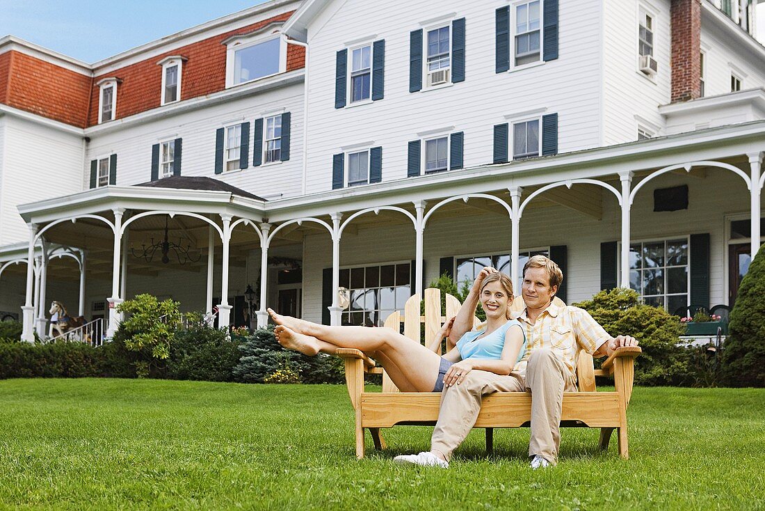 Verliebtes Paar auf einer Holzbank sitzend vor romantischem Hotel