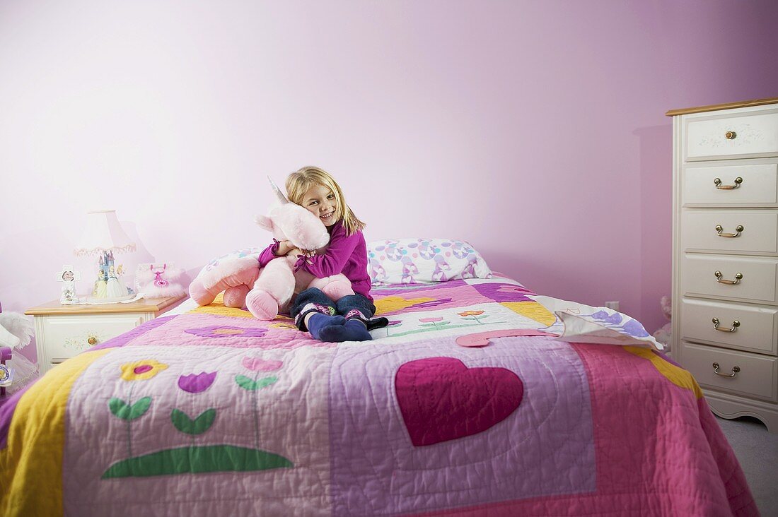 A girl sitting on her bed hugging a cuddly toy