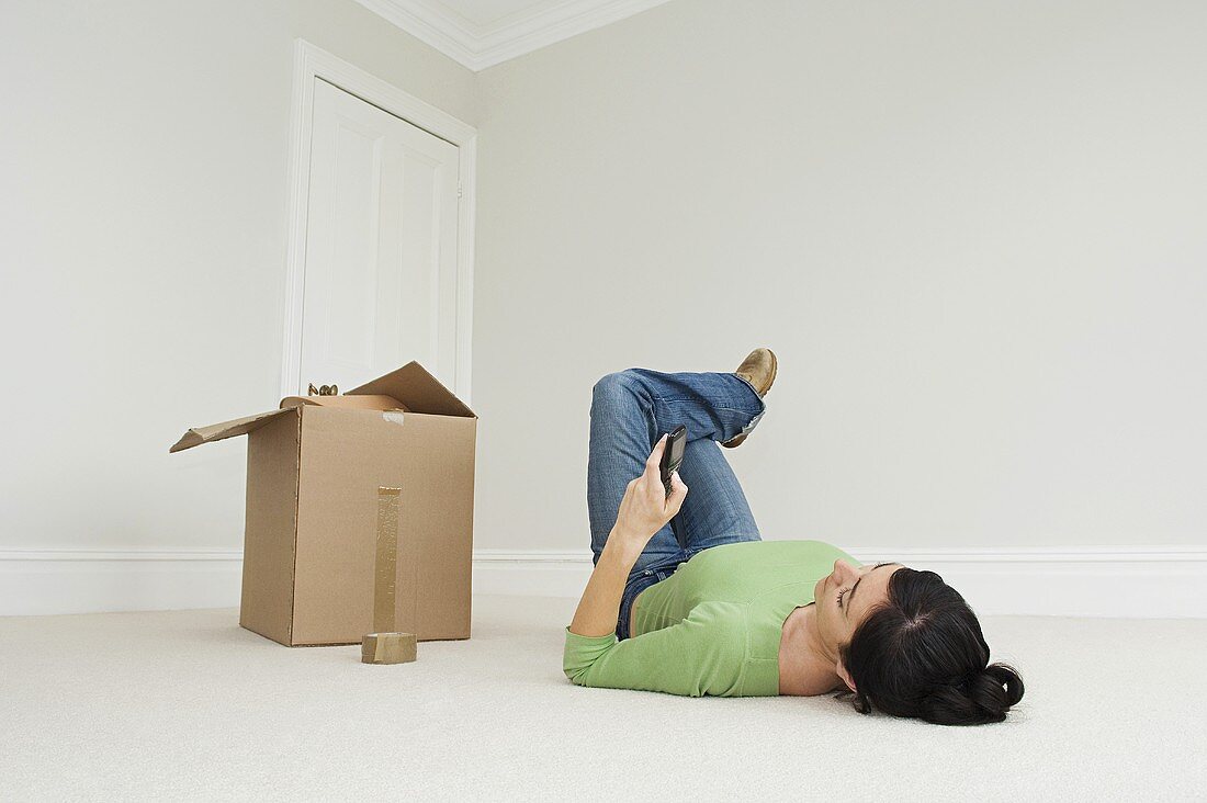 A woman on the phone lying on the floor next to a cardboard box