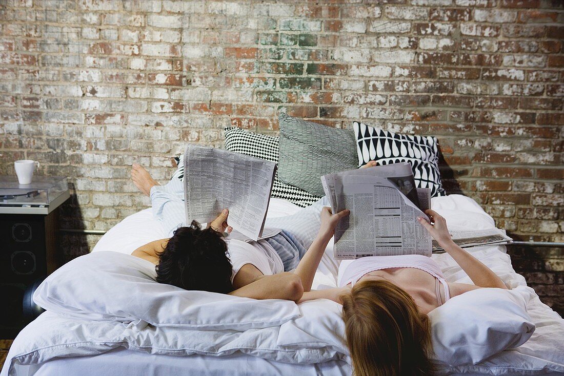 A couple reading newspapers in bed