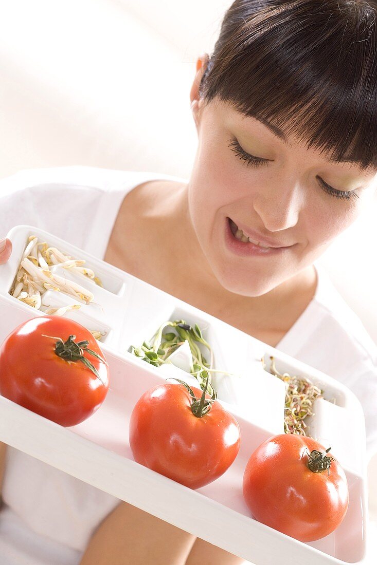 Junge Frau hält einen Teller mit Tomaten und Sprossen