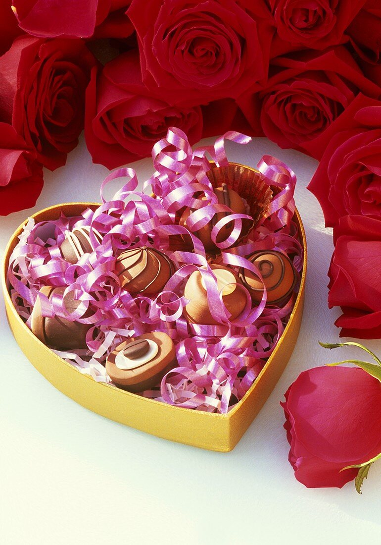Chocolates in heart-shaped box, red roses