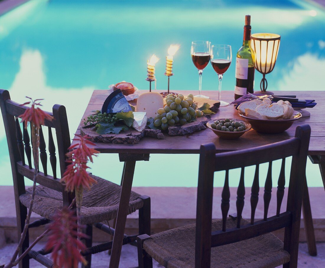 Tisch mit Käseplatte, Oliven, Weißbrot und Rotwein am Pool