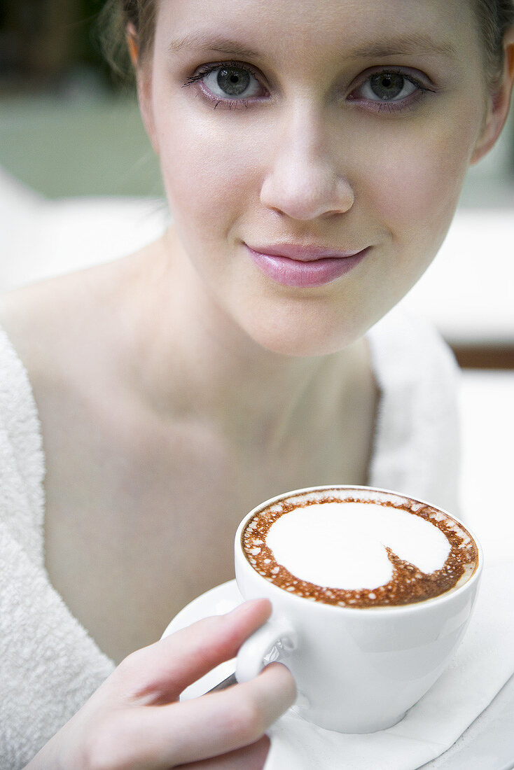 Young woman in bathrobe drinking cappuccino
