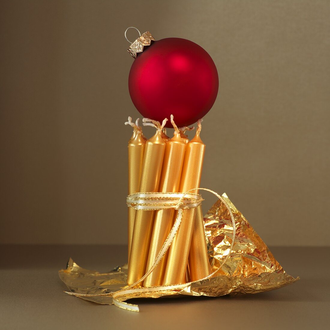 A red Christmas bauble balanced on golden candles