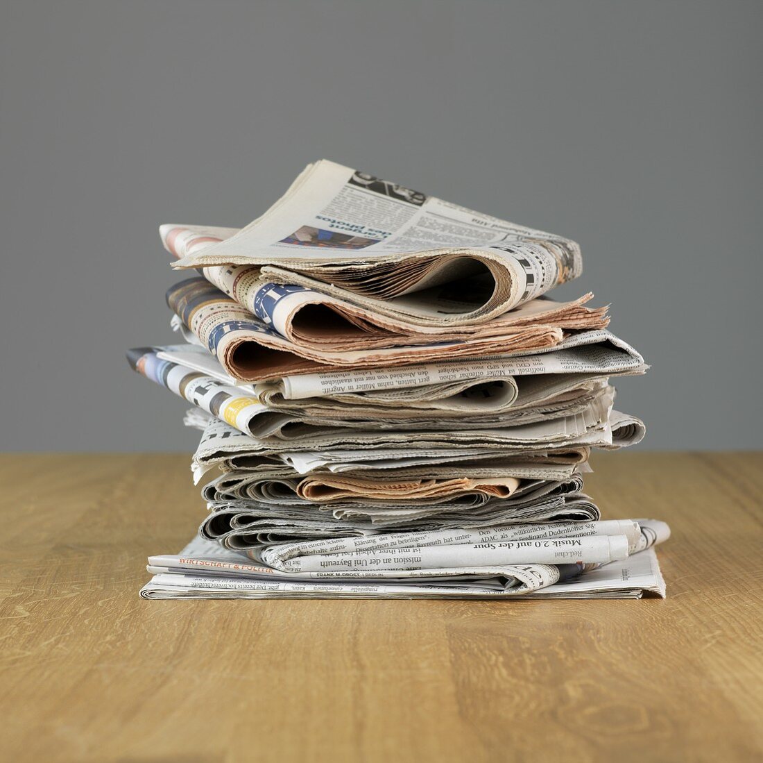 Zeitungsstapel auf Holzgrund vor grauer Wand