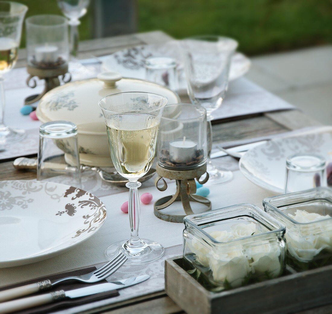 Gedeckter Tisch mit gefülltem Weinglas und Glasbehälter mit Blüten
