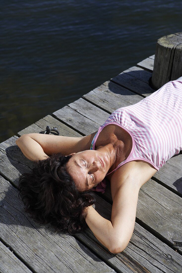 Frau sonnt sich auf Holzsteg am See