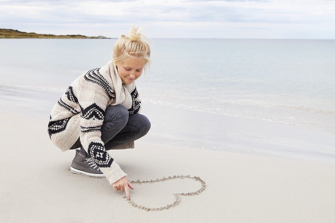 Teenager zeichnet Herz in den Sand am Meer