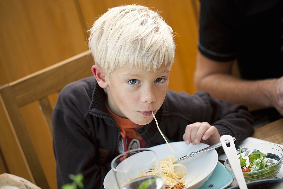 A blond boy eating spaghetti