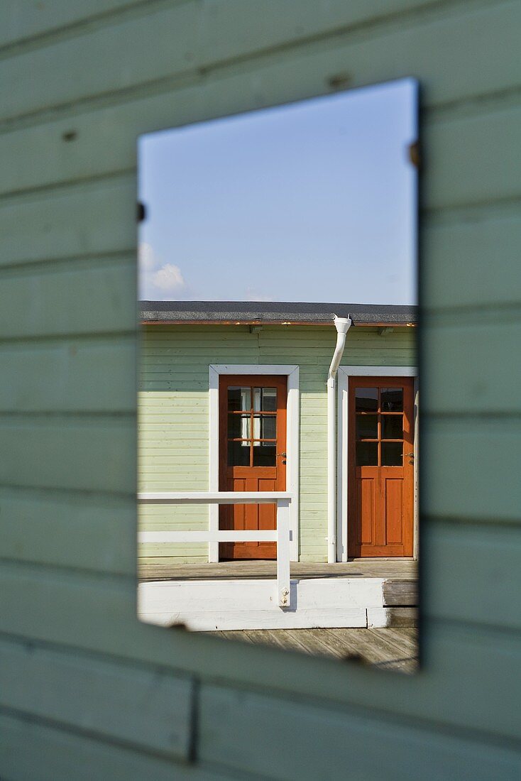 Holzhäuser spiegeln sich in einem an der Hausfassade aufgehängtem Wandspiegel
