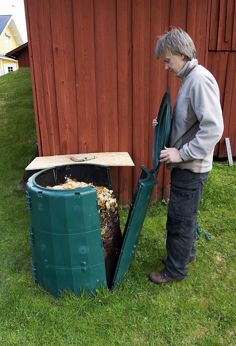 Mann öffnet gefüllte Komposttonne