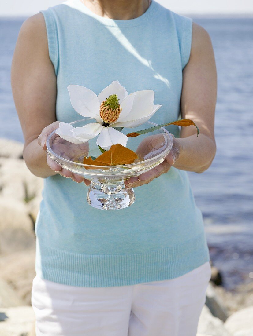 Frau hält Glasschale mit Blüten, Meer im Hintergrund