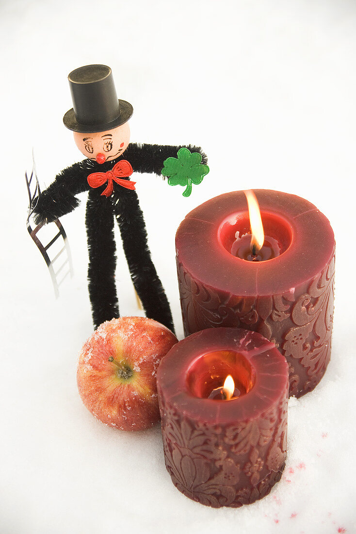 Schornsteinfeger, Apfel und rote Kerzen im Schnee