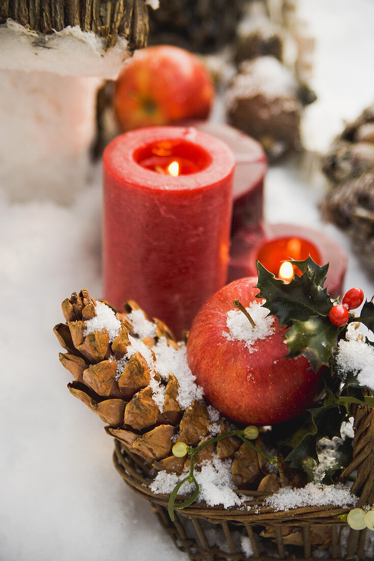 Weihnachtsdeko mit Äpfeln, Zapfen und Kerzen im Schnee