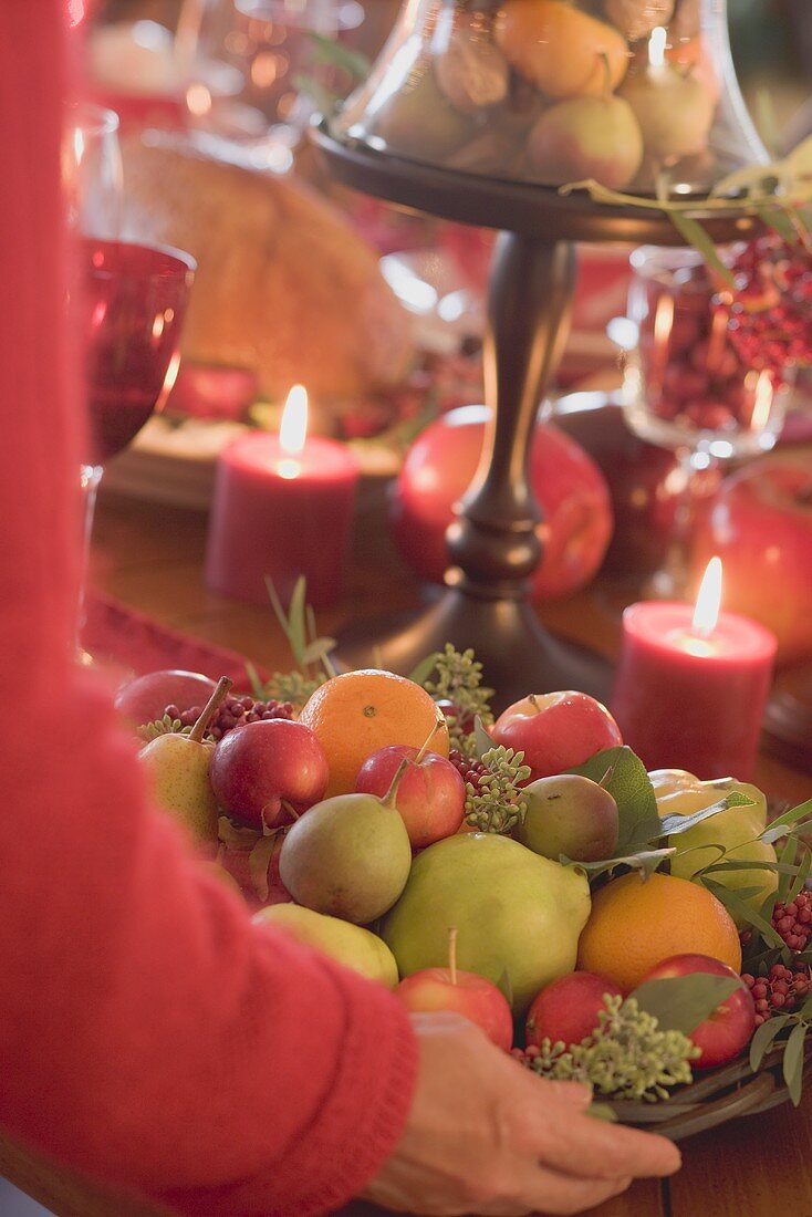 Woman placing bowl of fruit on table laid for Christmas