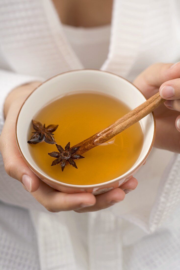 Woman holding bowl of tea with star anise & cinnamon stick