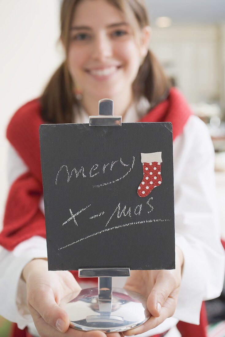 Junge Frau hält Tafel mit Aufschrift: Merry X-mas (Tischdeko)