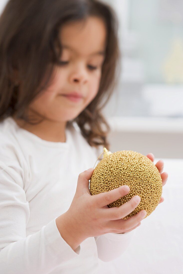 Kleines Mädchen hält goldene Christbaumkugel