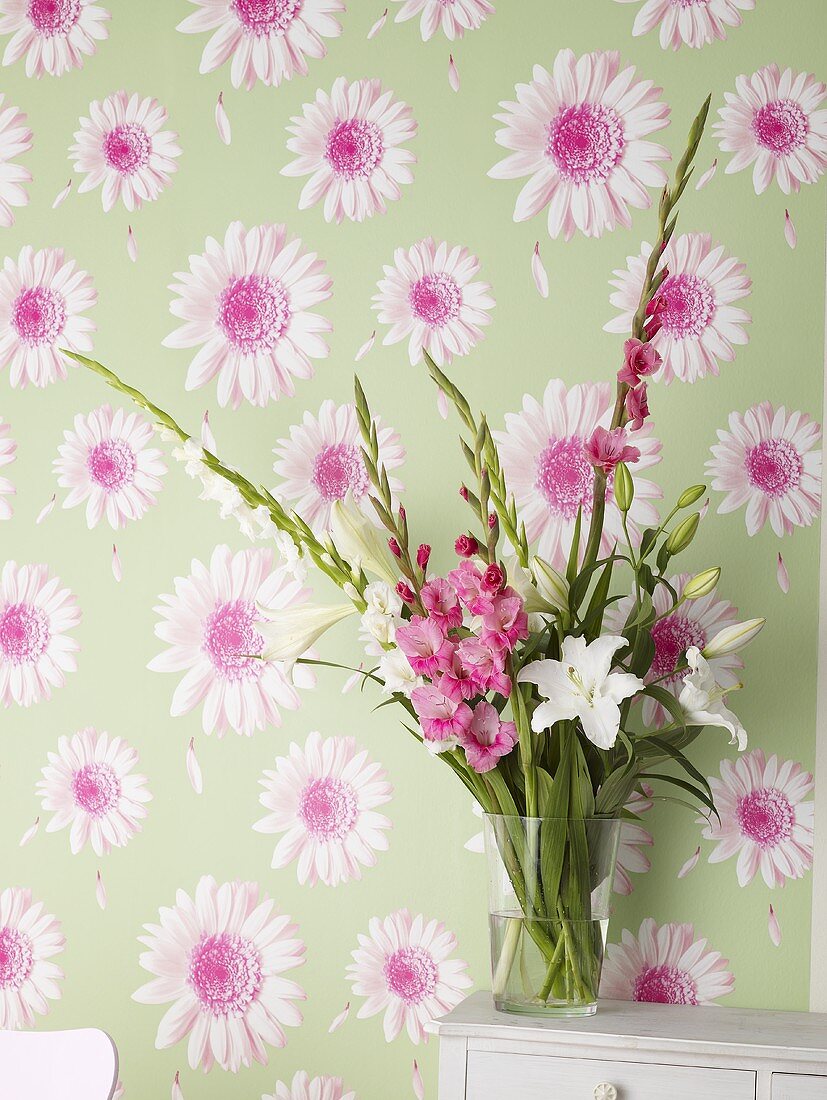 Vase of flowers against flowered wallpaper