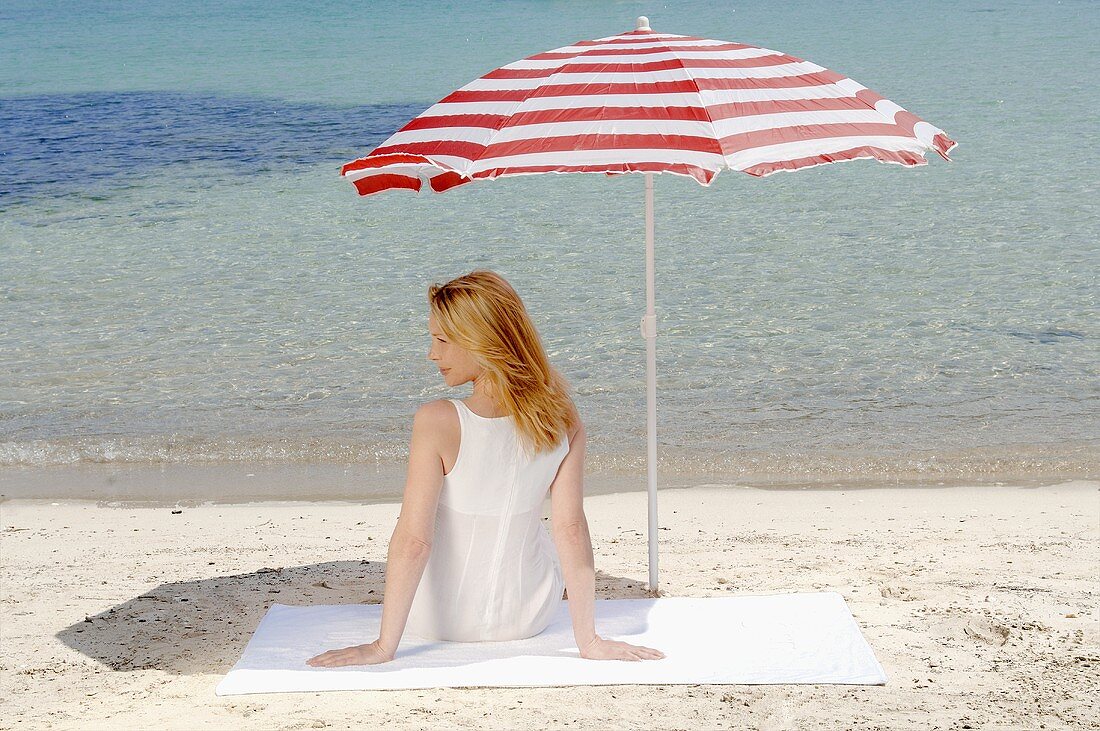 Frau sitzt am Strand unter Sonnenschirm