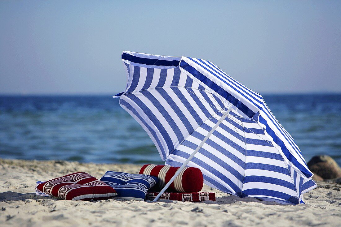 Blue & white beach umbrella & a few cushions on the beach