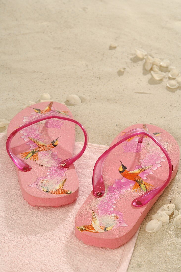 Pink flip-flops on a towel on sand
