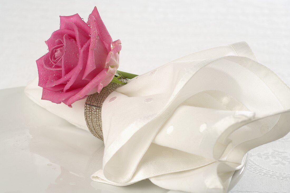 Stoffserviette mit pinkfarbener Rose auf weißem Teller
