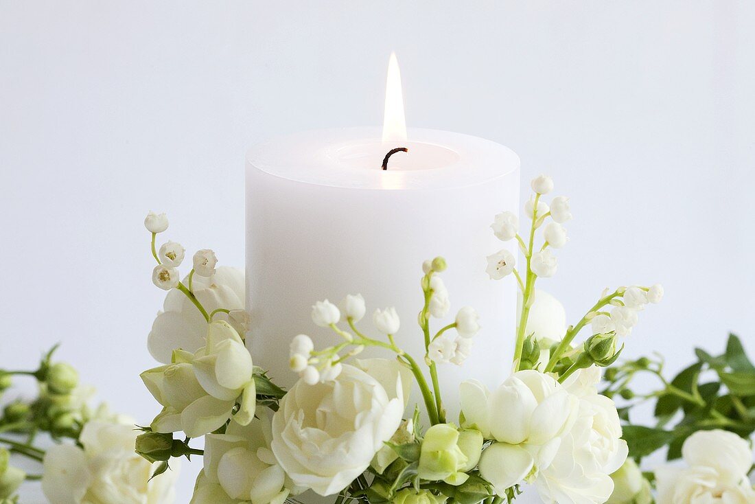 Brennende weiße Kerze mit weissen Rosen und Maiglöckchen
