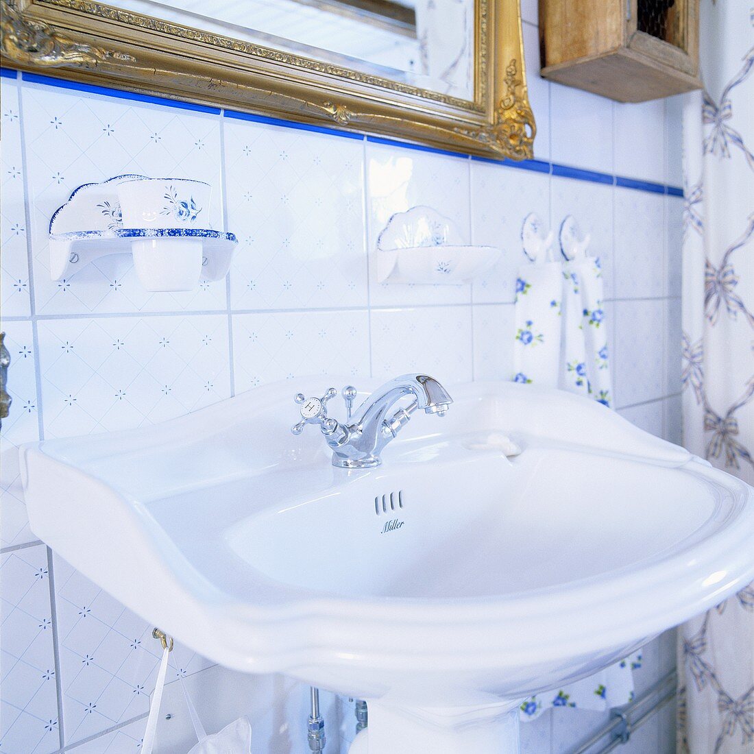 Nostalgisches Waschbecken in Badezimmer mit goldgerahmtem Spiegel und weiss-blauen Wandfliesen mit dezentem Blümchenmuster