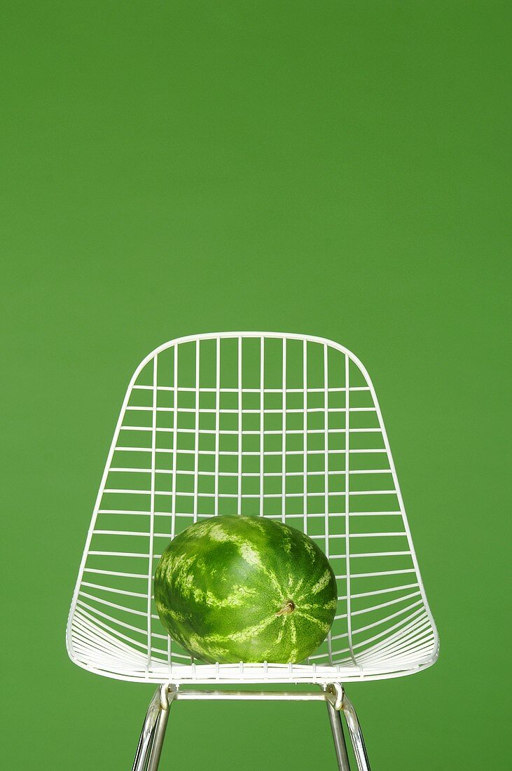 Wassermelone auf weißem Metallstuhl vor grüner Wand