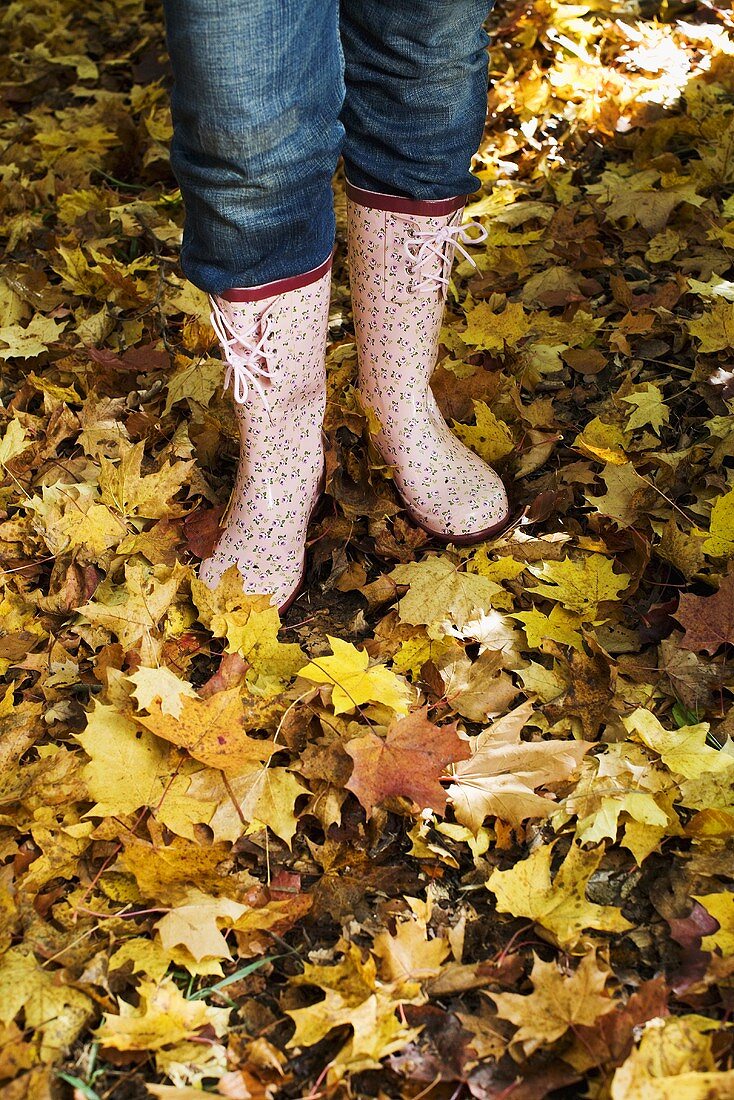 Frau steht mit Gummistiefeln auf Herbstlaub