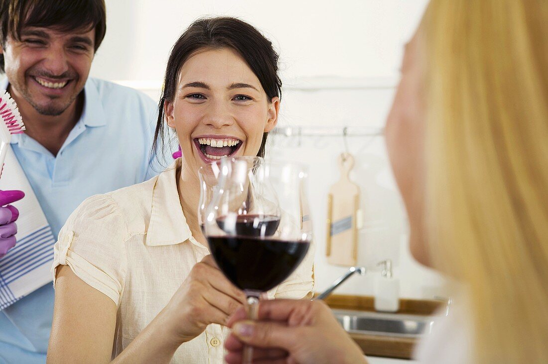 Three young people drinking wine in kitchen, smiling, close-up