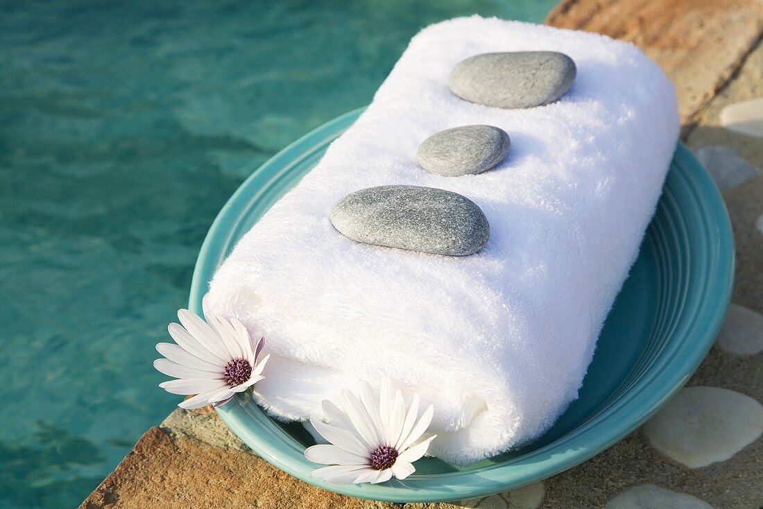 Towel, stones and flowers on plate by swimming pool