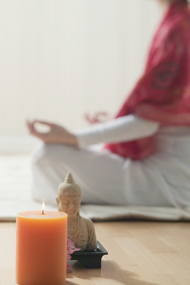 Frau im Yogasitz, Kerze und Buddhastatue