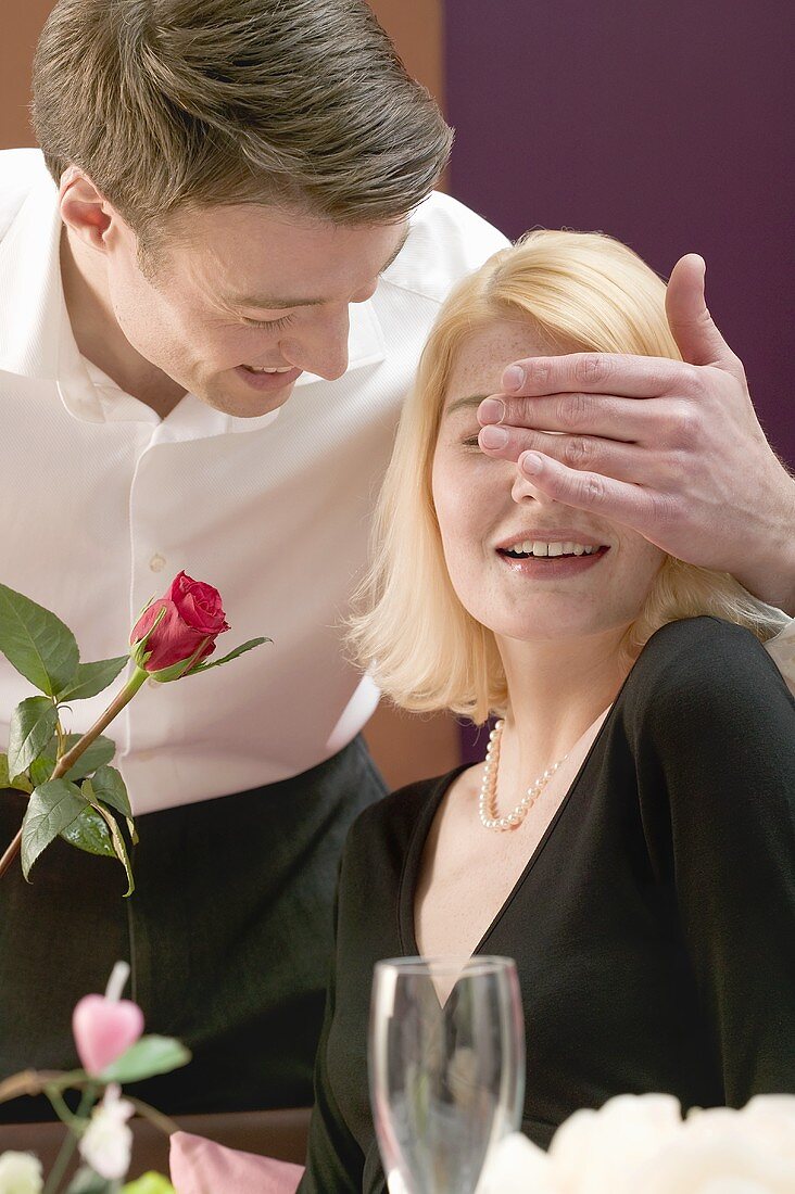 Mann überrascht Frau mit einer roten Rose