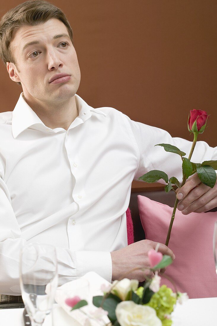 Einsamer Mann mit roter Rose im Restaurant