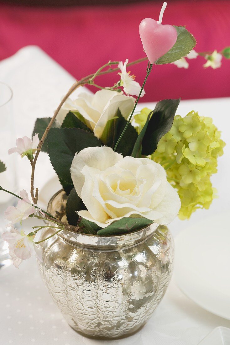 Blumenstrauss mit rosa Herz in Silbervase auf gedecktem Tisch