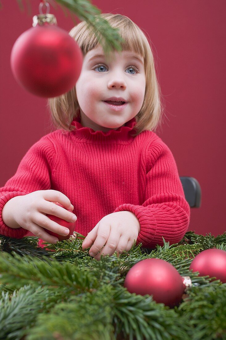 Kleines Mädchen schmückt Christbaum mit roten Kugeln