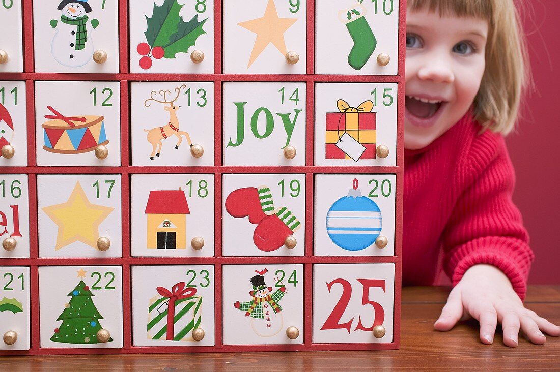 Small girl peeping out from behind Advent calendar