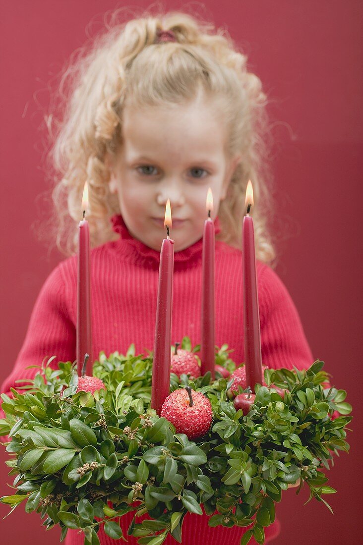Small girl holding Advent wreath with burning candles