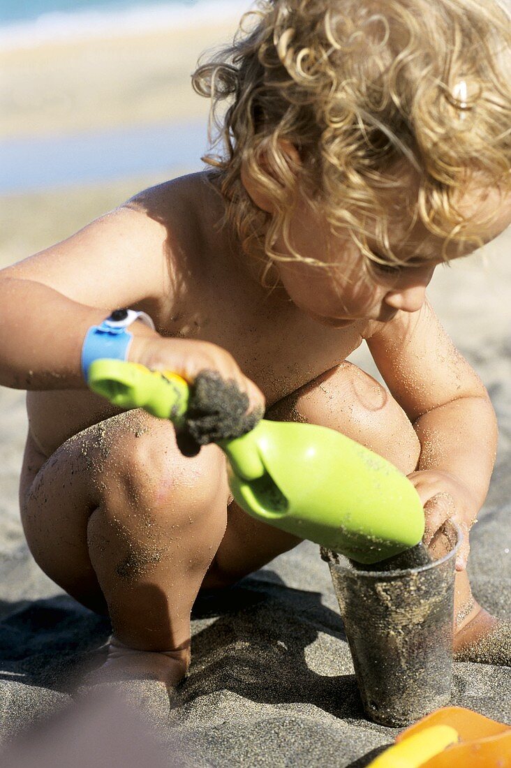 Kleines Mädchen schaufelt Sand in einen Becher