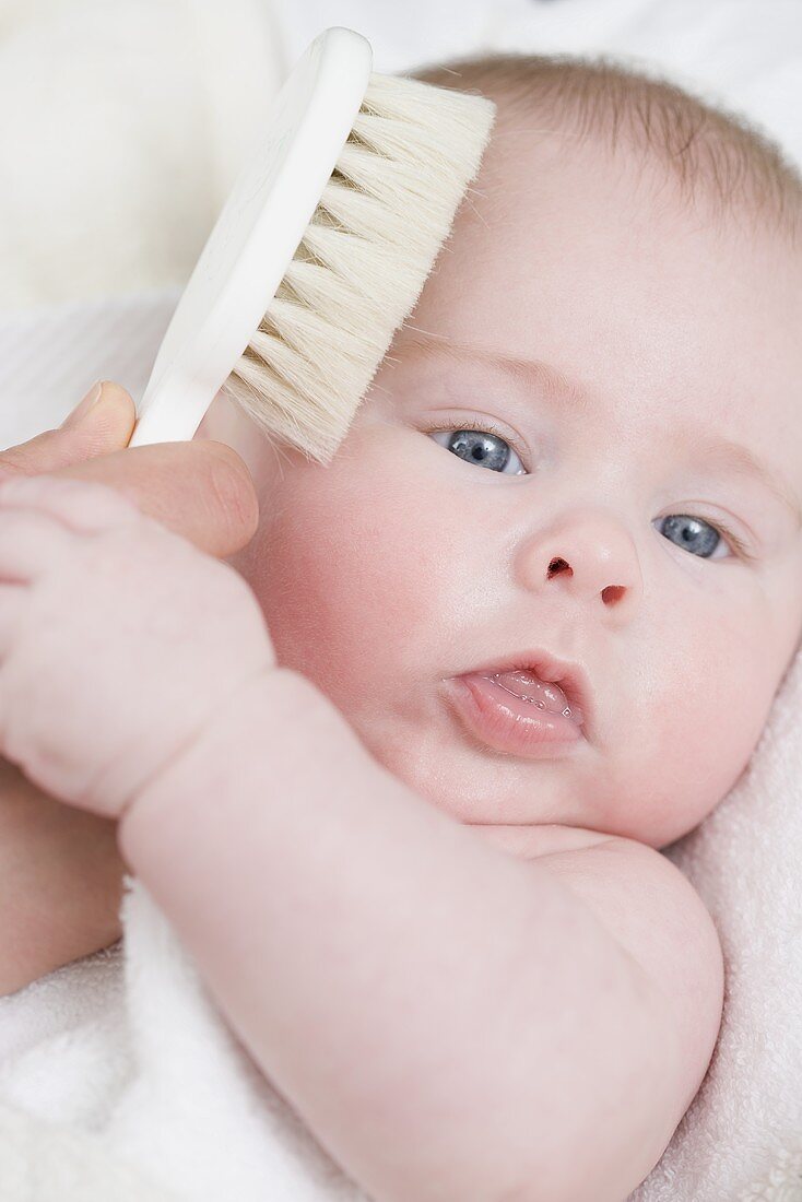 Hand brushing a baby's hair with a soft brush